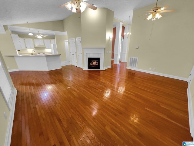 unfurnished living room featuring wood-type flooring, sink, a textured ceiling, high vaulted ceiling, and ceiling fan