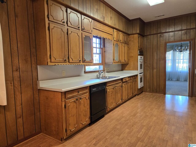 kitchen featuring black dishwasher, a sink, wooden walls, double oven, and light wood-style flooring