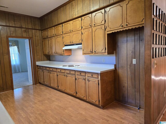 kitchen featuring wood walls, under cabinet range hood, light wood-style floors, light countertops, and brown cabinetry