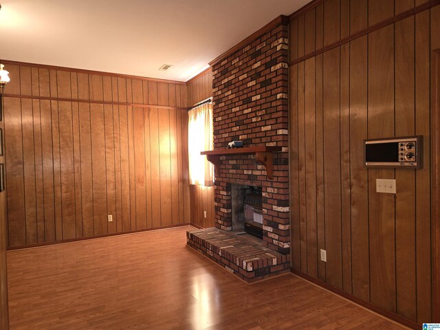 living room with wood finished floors, a brick fireplace, wood walls, and baseboards