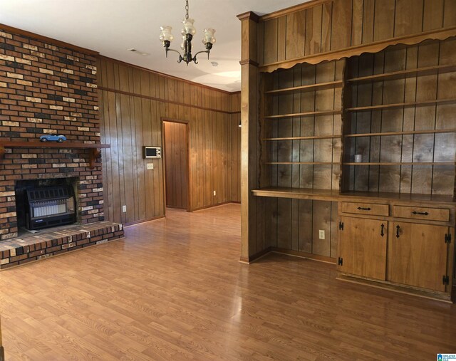 unfurnished living room featuring wood walls, a chandelier, wood finished floors, a fireplace, and crown molding
