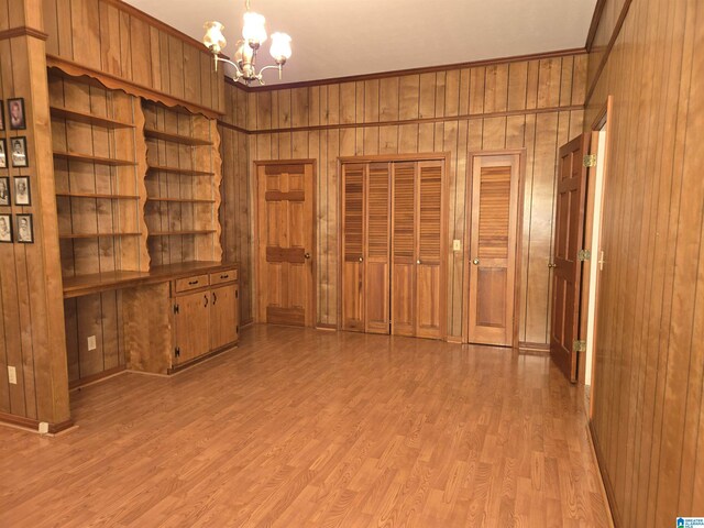 empty room featuring a chandelier, wood walls, light wood-type flooring, and ornamental molding