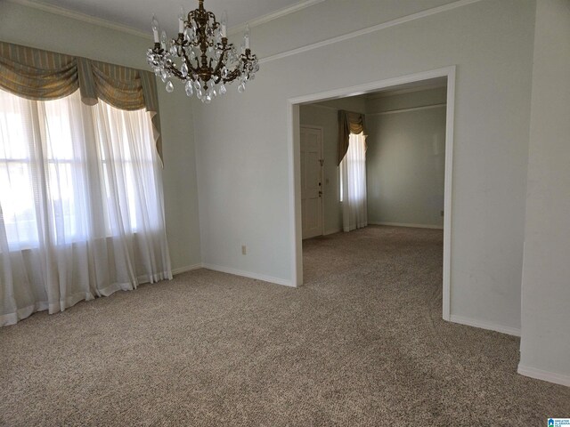 carpeted empty room featuring a chandelier, crown molding, and baseboards