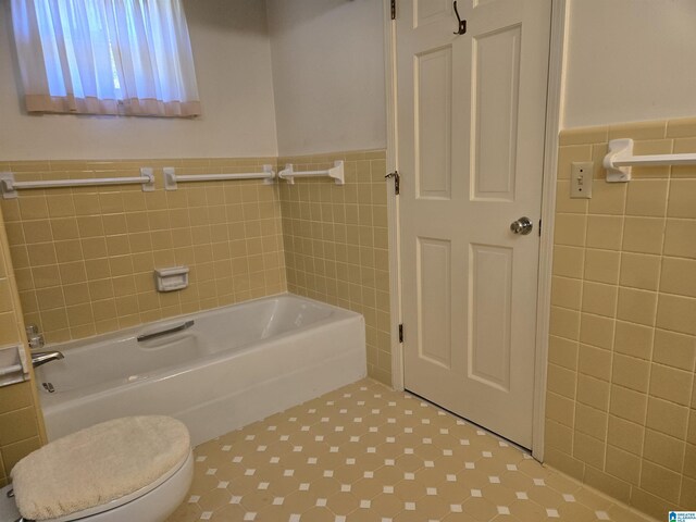bathroom featuring tile walls, a bathtub, wainscoting, and toilet
