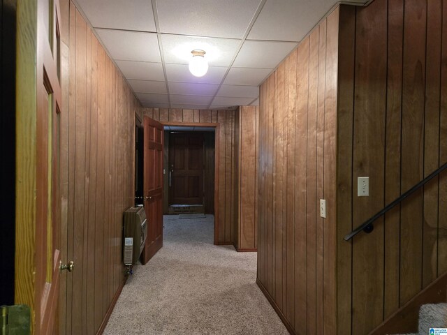hallway featuring heating unit, light colored carpet, wood walls, and a drop ceiling