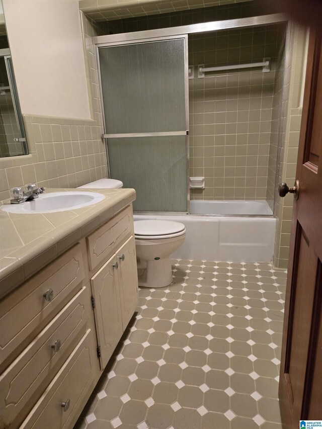 full bath with tile patterned floors, vanity, toilet, combined bath / shower with glass door, and tile walls