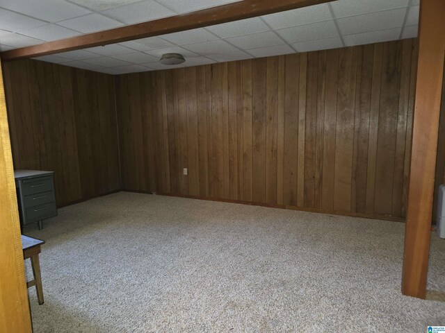 finished basement featuring wooden walls, a drop ceiling, and carpet floors