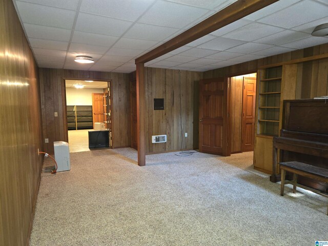 basement featuring wood walls, carpet flooring, and a paneled ceiling