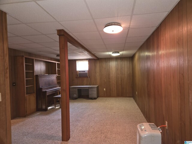 basement featuring carpet floors, wooden walls, an office area, a drop ceiling, and cooling unit