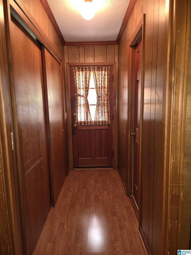 doorway to outside with wood finished floors, wood walls, and ornamental molding