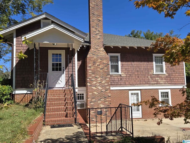 view of front facade featuring a chimney, a shingled roof, and brick siding