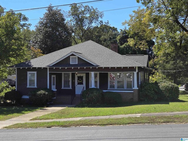 bungalow with roof with shingles, covered porch, a chimney, and a front yard
