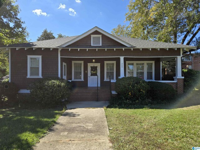view of front facade featuring a porch, roof with shingles, and a front yard