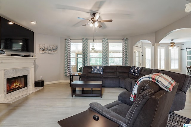 living room with ceiling fan, a healthy amount of sunlight, light hardwood / wood-style flooring, and a high end fireplace