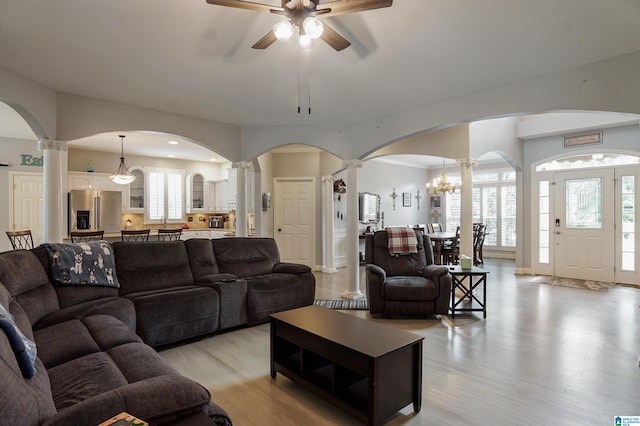 living room with light hardwood / wood-style flooring, ceiling fan with notable chandelier, plenty of natural light, and decorative columns