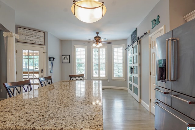 kitchen featuring light wood-type flooring, ceiling fan, high quality fridge, light stone counters, and a breakfast bar area