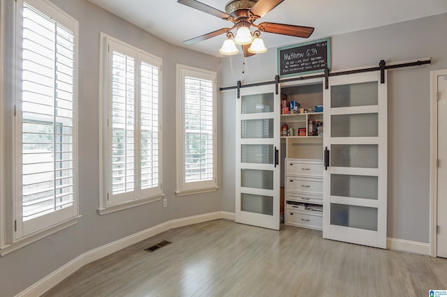 unfurnished bedroom featuring ceiling fan, light wood-type flooring, and a barn door