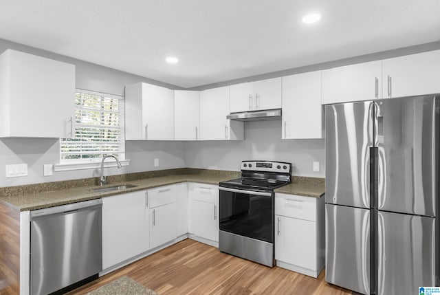 kitchen with white cabinets, appliances with stainless steel finishes, dark stone countertops, light hardwood / wood-style floors, and sink