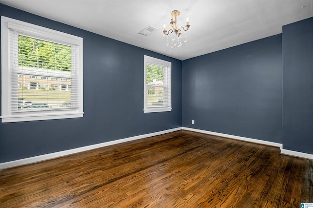 spare room with a notable chandelier and dark hardwood / wood-style flooring