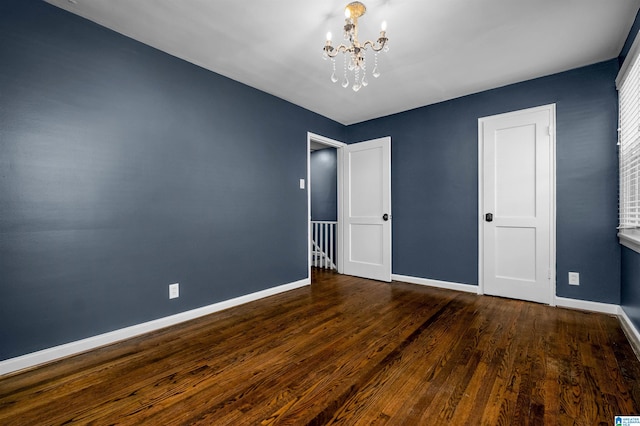 unfurnished bedroom with dark wood-type flooring and an inviting chandelier