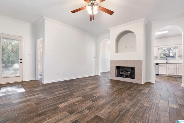 unfurnished living room featuring ornamental molding, sink, dark hardwood / wood-style flooring, a fireplace, and ceiling fan