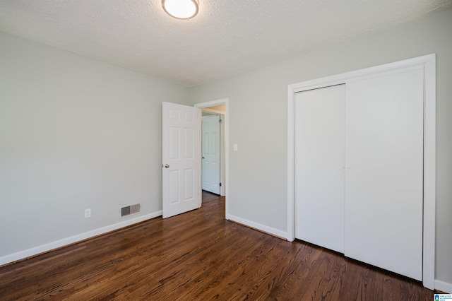 unfurnished bedroom with a closet, a textured ceiling, and dark wood-type flooring