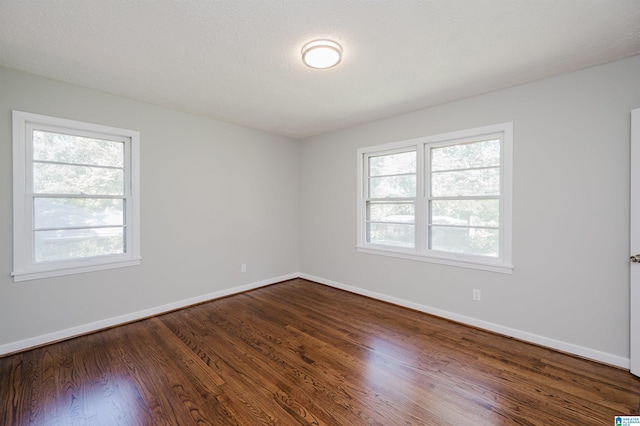 unfurnished room featuring a textured ceiling, a healthy amount of sunlight, and dark hardwood / wood-style flooring