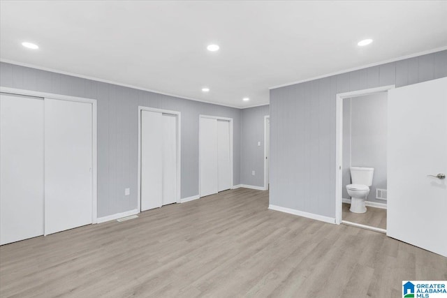 unfurnished bedroom with ensuite bathroom, multiple closets, and light hardwood / wood-style floors