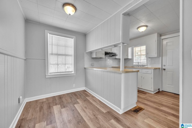 kitchen featuring tasteful backsplash, kitchen peninsula, white cabinetry, ornamental molding, and light hardwood / wood-style flooring