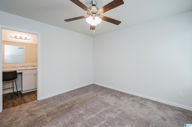 empty room featuring built in desk, ceiling fan, and dark colored carpet