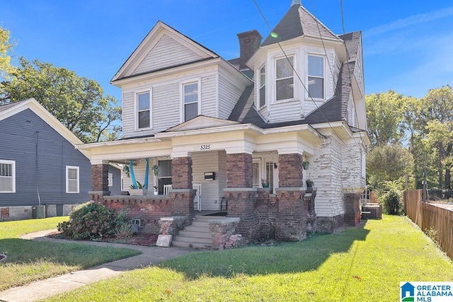 victorian house featuring central AC, covered porch, and a front lawn