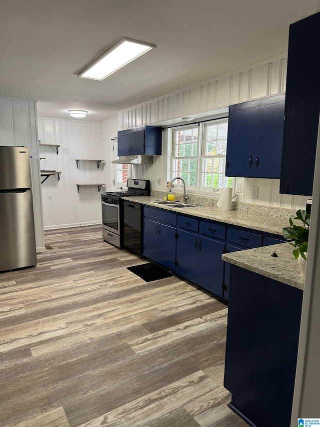 kitchen featuring appliances with stainless steel finishes, sink, blue cabinets, light stone counters, and light hardwood / wood-style flooring