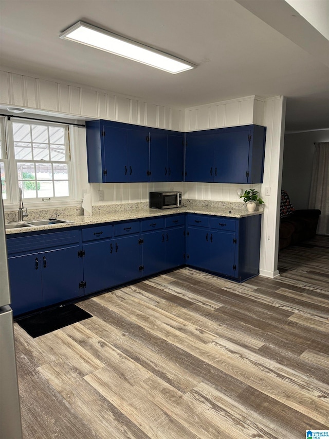 kitchen with dark wood-type flooring, blue cabinetry, light stone countertops, and sink