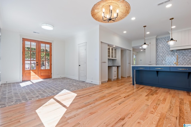 kitchen with pendant lighting, french doors, decorative backsplash, light wood-type flooring, and a notable chandelier