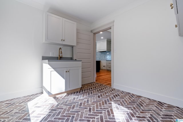 bar with backsplash, white cabinetry, and sink