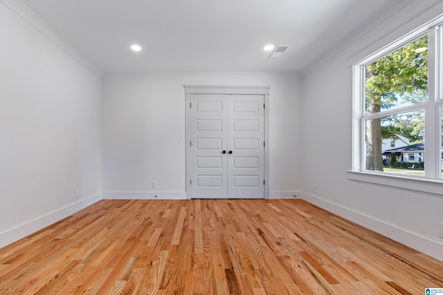 unfurnished bedroom featuring light hardwood / wood-style floors, crown molding, and a closet