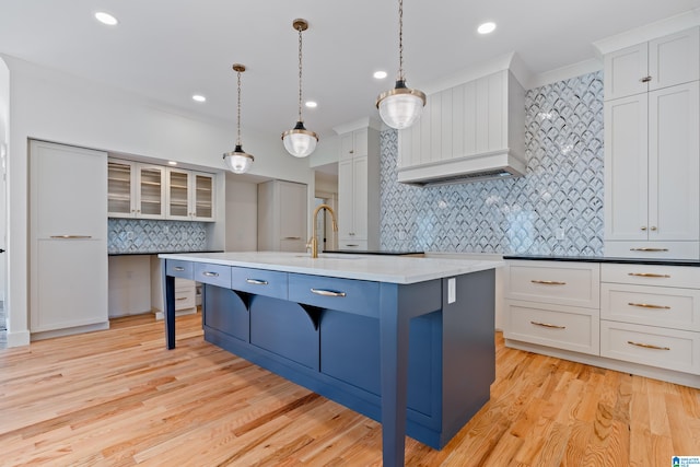 kitchen featuring decorative backsplash, light wood-type flooring, a center island with sink, white cabinets, and hanging light fixtures