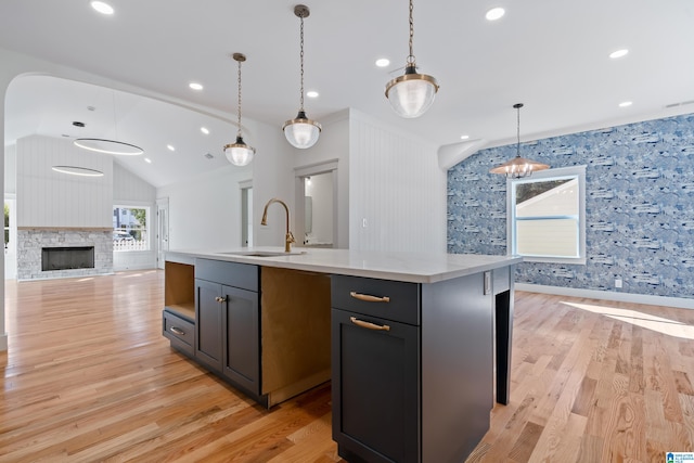 kitchen with a center island with sink, sink, hanging light fixtures, and light hardwood / wood-style flooring