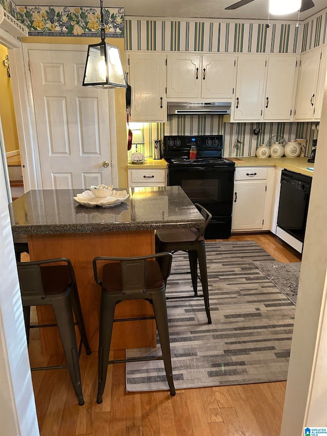 kitchen with white cabinets, a kitchen breakfast bar, light hardwood / wood-style flooring, black appliances, and pendant lighting