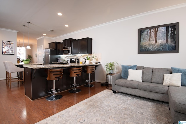 kitchen featuring stainless steel appliances, decorative light fixtures, dark wood-type flooring, crown molding, and a breakfast bar