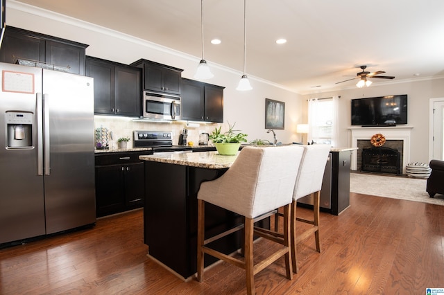 kitchen featuring appliances with stainless steel finishes, an island with sink, a kitchen bar, and hanging light fixtures