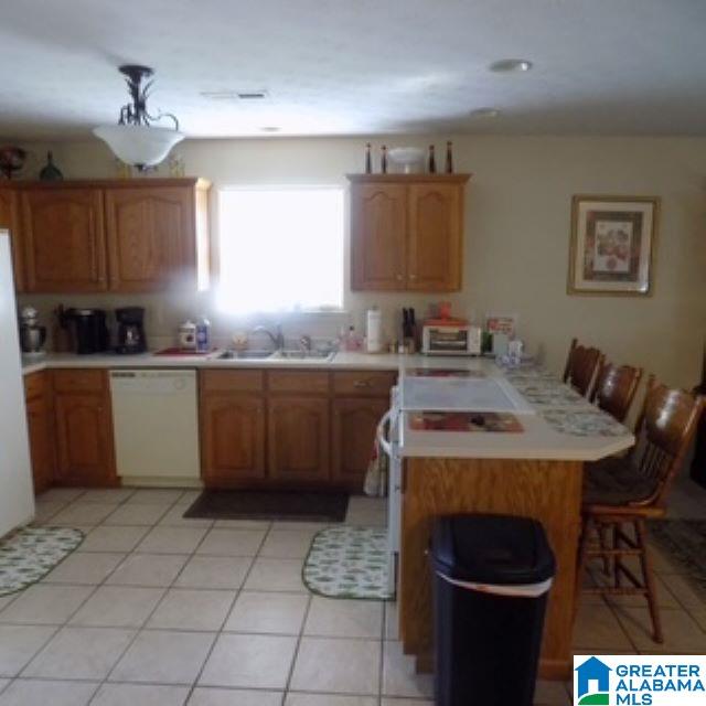 kitchen with kitchen peninsula, light tile patterned floors, white dishwasher, a kitchen bar, and sink