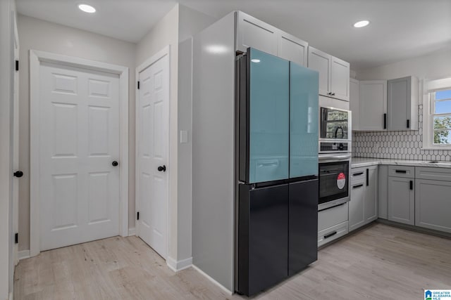 kitchen featuring appliances with stainless steel finishes, gray cabinetry, backsplash, and light hardwood / wood-style floors