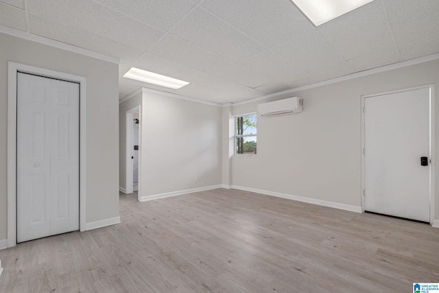 empty room featuring a drop ceiling, ornamental molding, a wall mounted AC, and light wood-type flooring