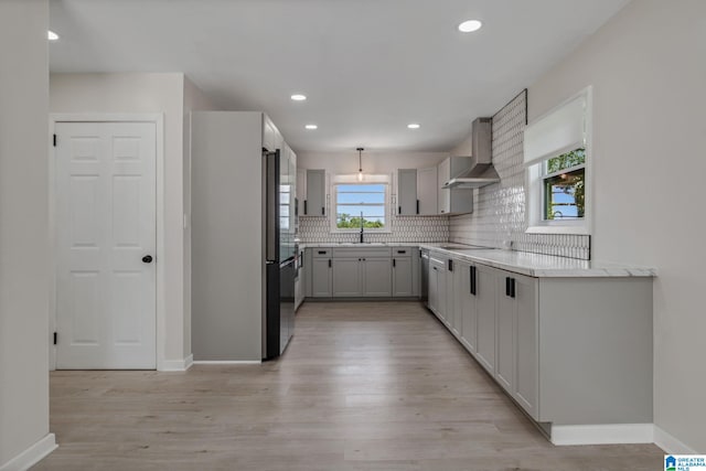 kitchen with wall chimney range hood, light hardwood / wood-style flooring, and plenty of natural light