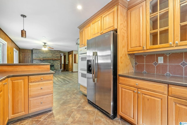 kitchen with stainless steel fridge, ceiling fan, a brick fireplace, decorative light fixtures, and white double oven