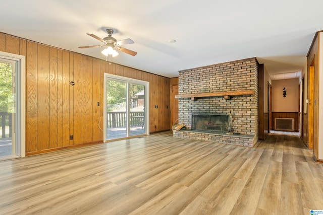 unfurnished living room featuring wooden walls, a fireplace, light hardwood / wood-style floors, and plenty of natural light