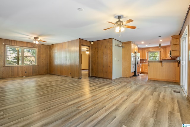 unfurnished living room featuring light hardwood / wood-style flooring, ceiling fan, and wood walls