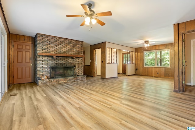 unfurnished living room with light hardwood / wood-style floors, a brick fireplace, wooden walls, and ceiling fan