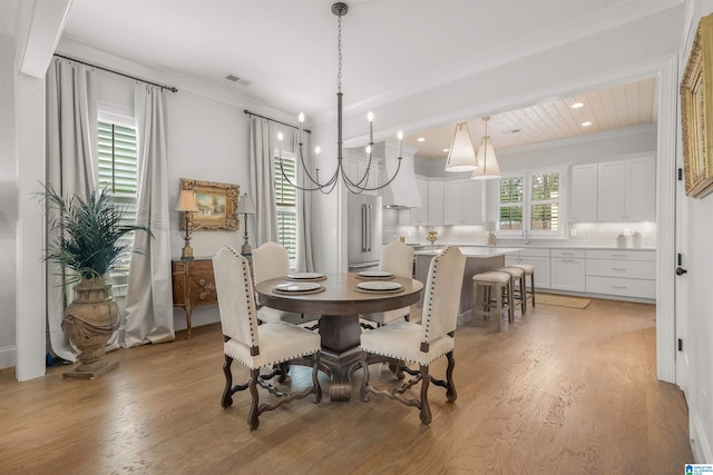 dining area with ornamental molding, a notable chandelier, and light hardwood / wood-style floors